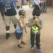 shows two boys holding their white canes and wearing sleep shades.