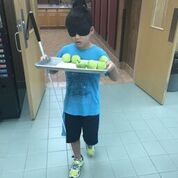shows a boy with his white cane and wearing sleep shades as he carries a tray of green apples.