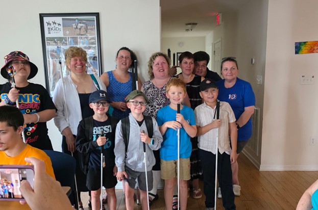 Six mentors and five students with white canes smile together