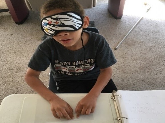 shows a boy in sleep shades reading the Braille letter he just received in the mail.