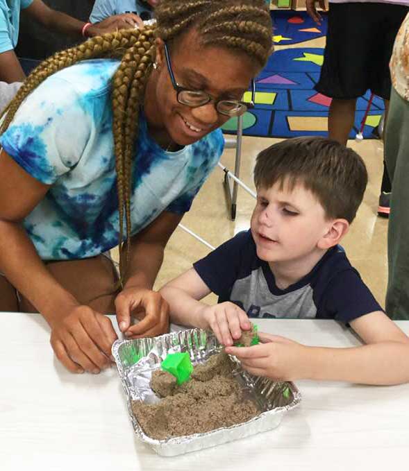 shows a volunteer and a BELL student as they make models of sand castles using kinetic sand.
